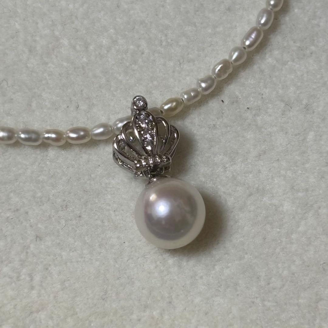 Pearl and silver double necklace with crown motif pendant and lobster clasp on white background