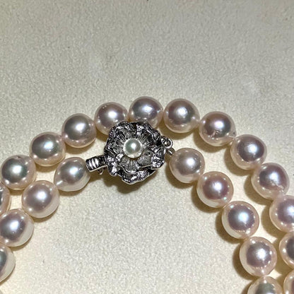 Akoya pearl necklace with white to light pink 8.0mm pearls and silver flower motif clasp on white background