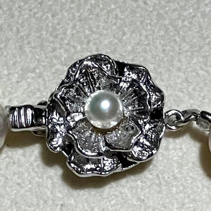 Akoya pearl necklace with white to light pink 8.0mm pearls and silver flower motif clasp on white background
