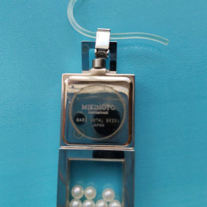 Mikimoto pendant head with decorative pearls, non-working watch, and ballpoint pen set on white background