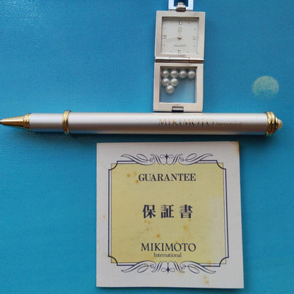 Mikimoto pendant head with decorative pearls, non-working watch, and ballpoint pen set on white background