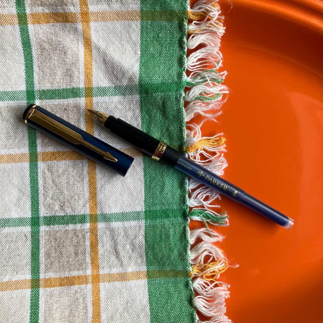 Cross black matte ballpoint pen with silver accents next to Parker blue and black fountain pen with gold nib engraving 88