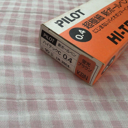 Pilot Hi-Tech C ballpoint pen in fluorescent brown with visible signs of wear and discoloration