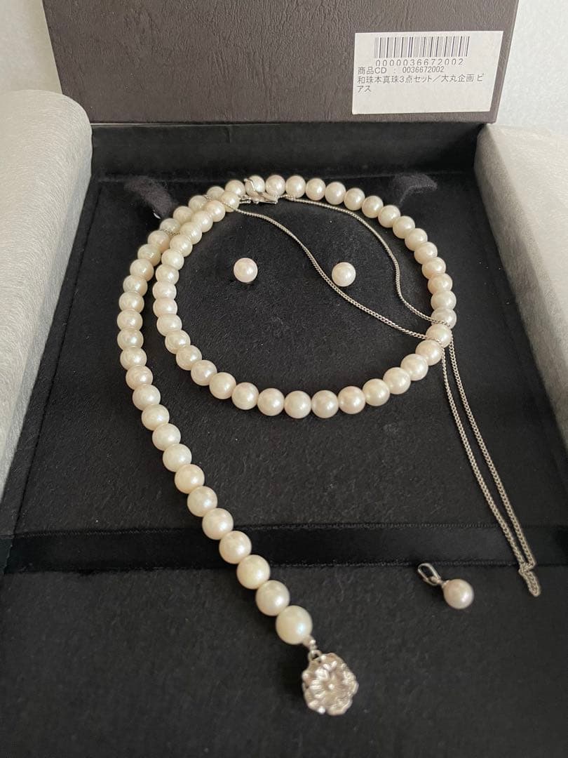 Akoya pearl necklace, earrings, and pendant set with white round pearls and silver chains on white background