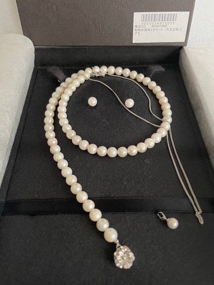 Akoya pearl necklace, earrings, and pendant set with white round pearls and silver chains on white background