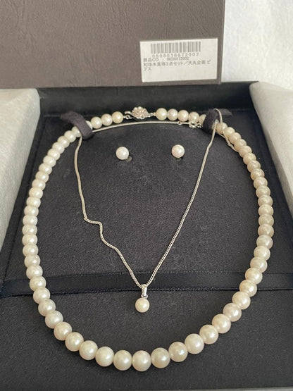 Akoya pearl necklace, earrings, and pendant set with white round pearls and silver chains on white background