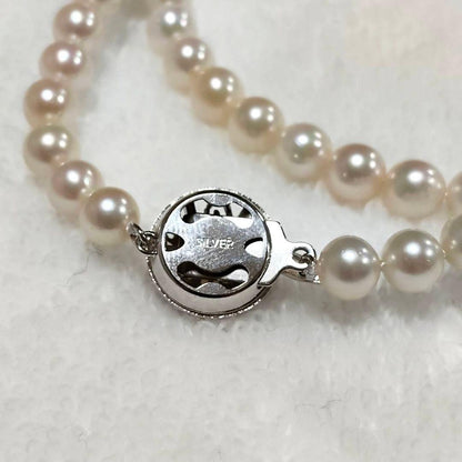 Akoya pearl necklace with 4-7mm white pearls and silver stamp clasp on a white background