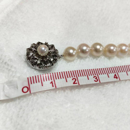 Akoya pearl necklace with 4-7mm white pearls and silver stamp clasp on a white background