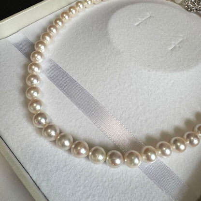Akoya pearl necklace with white to pink pearls and silver metal fittings displayed on white background