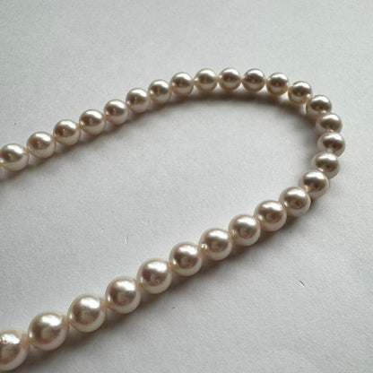 Akoya pearl necklace with white to pink pearls and silver metal fittings displayed on white background