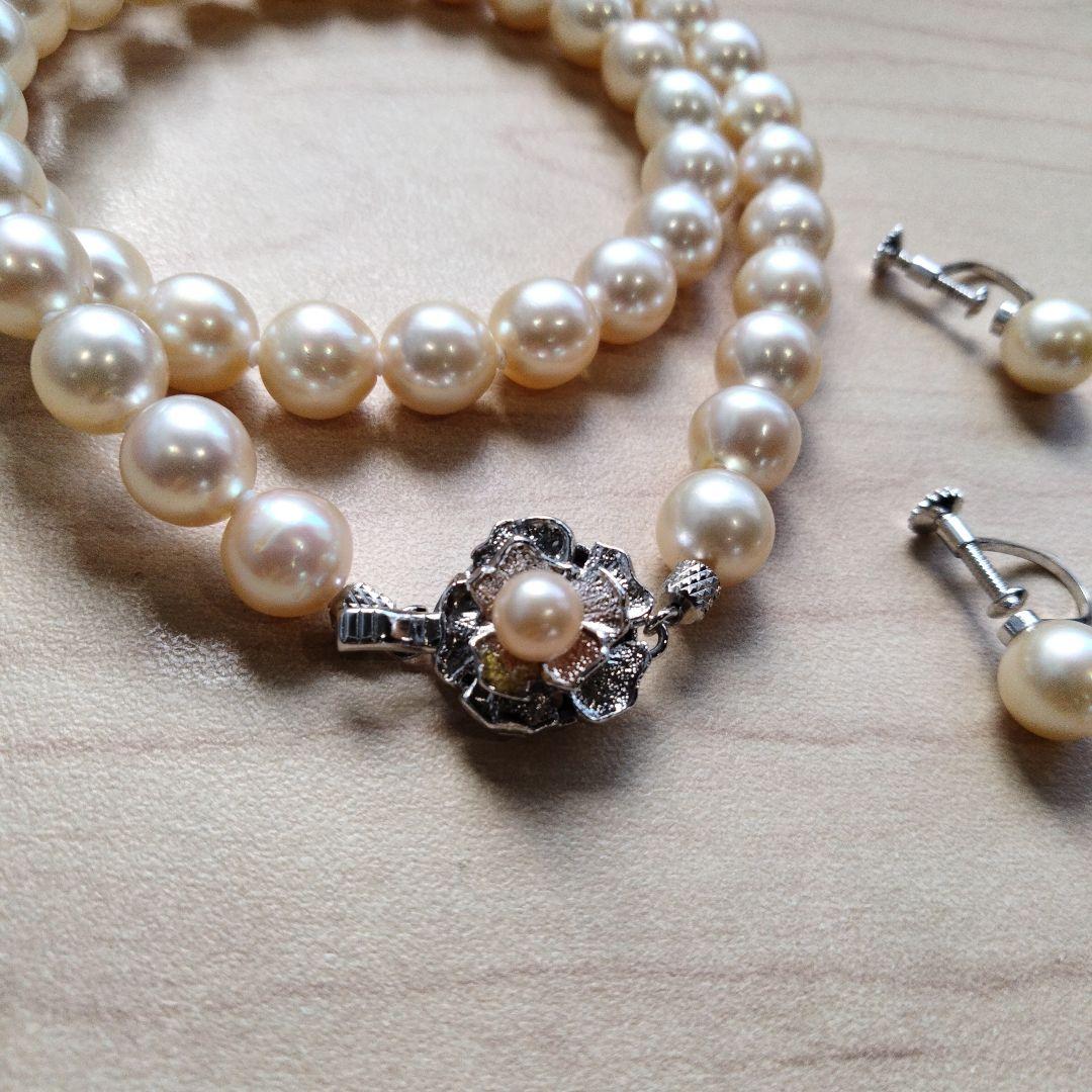 Akoya pearl necklace and matching earrings set with white pearls and silver clasp on a white background