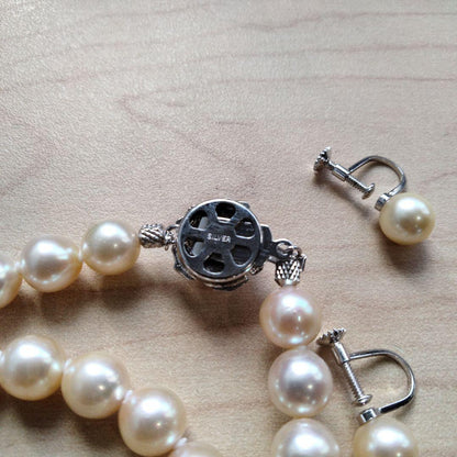 Akoya pearl necklace and matching earrings set with white pearls and silver clasp on a white background