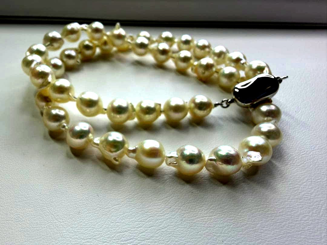 Akoya pearl necklace with 7.5mm white pearls and silver clasp laid flat on white background