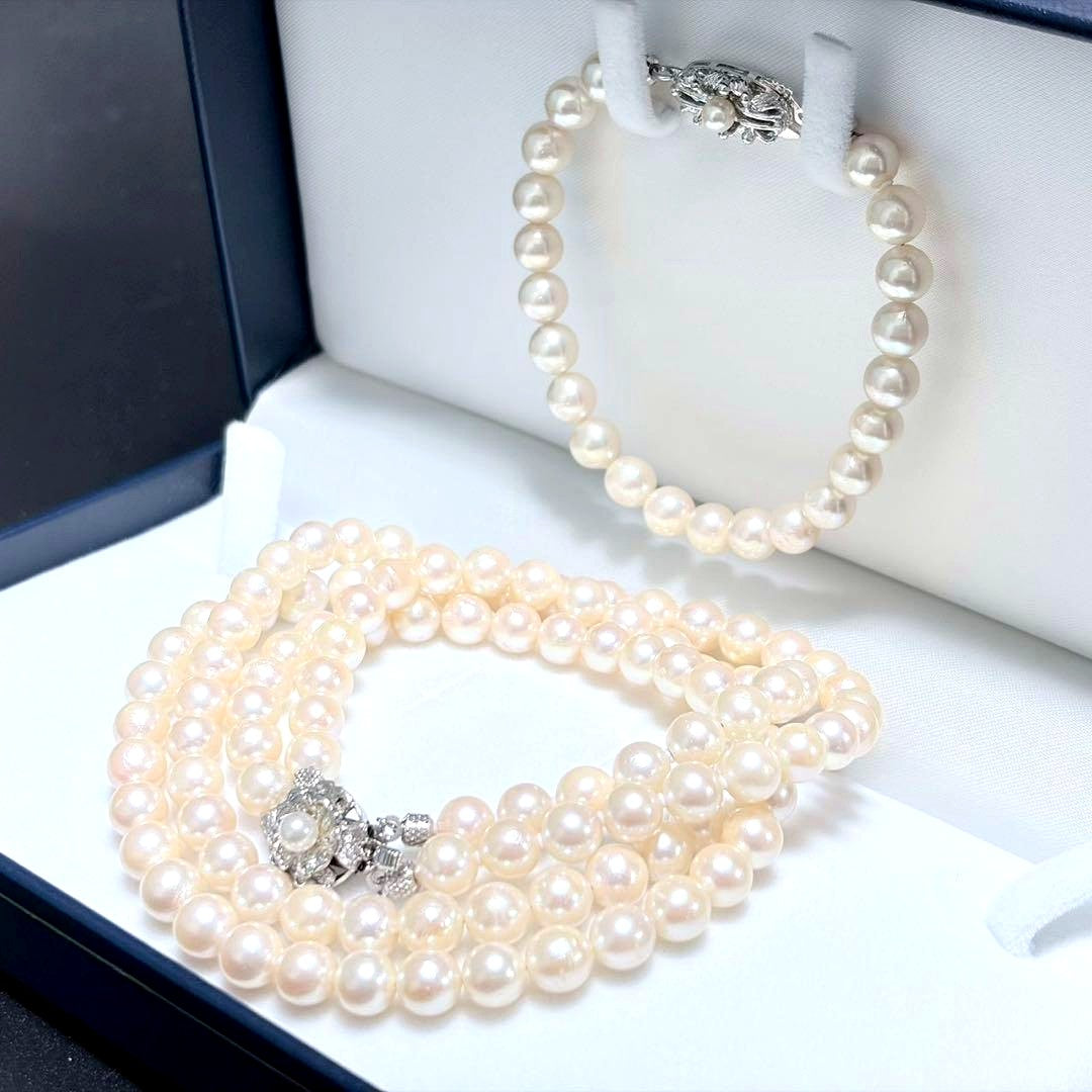 Akoya pearl double strand necklace and matching bracelet with silver clasp laid out on white background