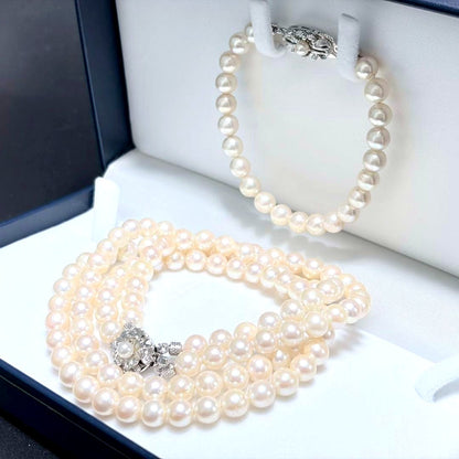 Akoya pearl double strand necklace and matching bracelet with silver clasp laid out on white background