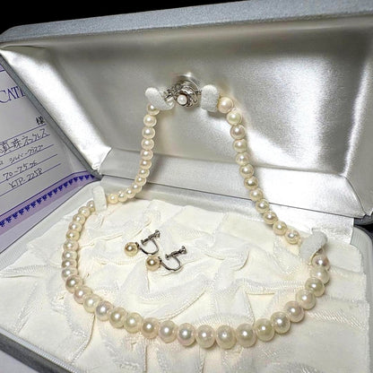 Akoya pearl necklace and matching earrings with silver engraved flower clasp on a white background