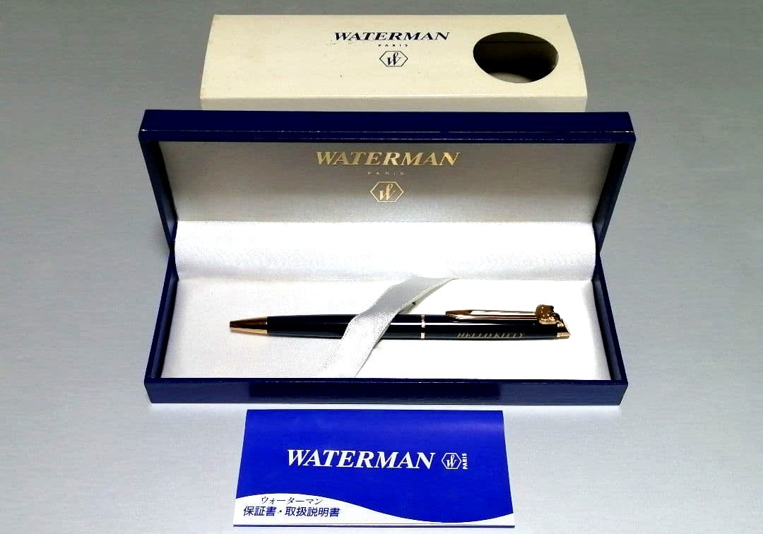 Hello Kitty Waterman ballpoint pen with extra ink refill, external box, and vintage storage case showing yellowing