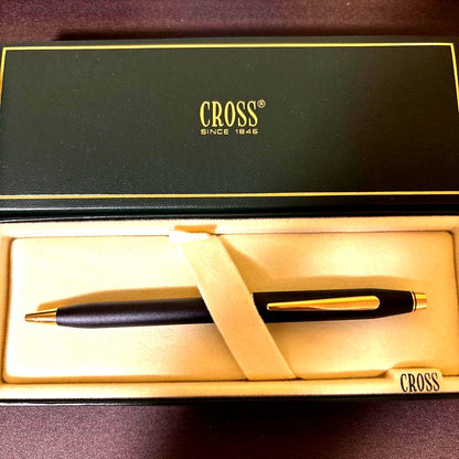 CROSS ballpoint pen with matte black barrel and gold clip lying on white background