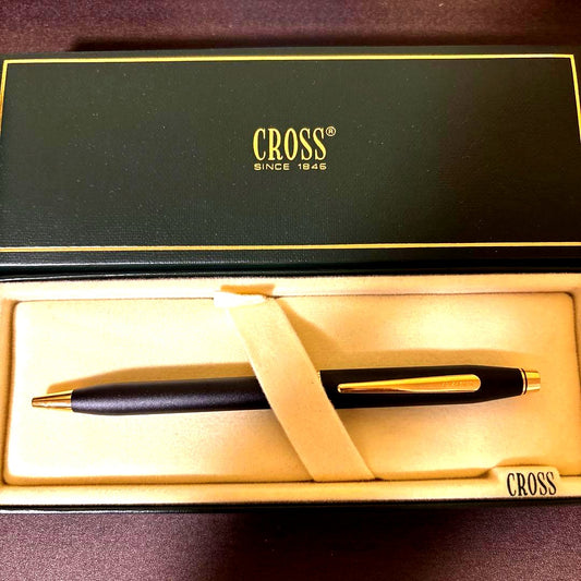 CROSS ballpoint pen with matte black barrel and gold clip lying on white background