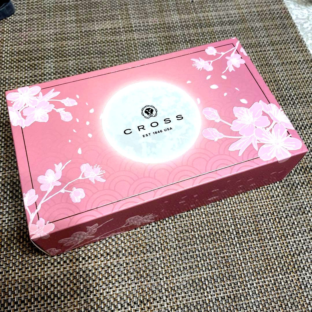 Cross Sakura pink ballpoint pen with cherry blossom pattern next to its cherry blossom design and black box packaging
