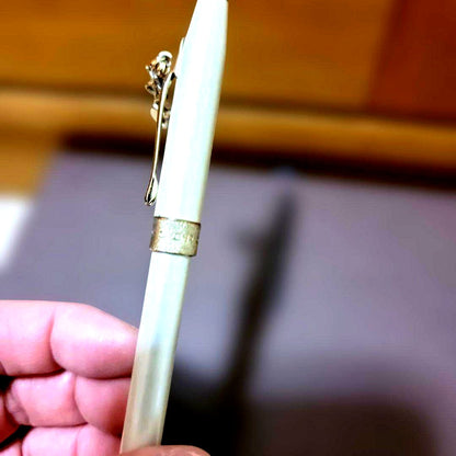 Cross ballpoint pen with pearl white metal body, gold trim, textured center ring, and heart-shaped charm clip