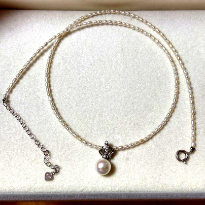 Pearl and silver double necklace with crown motif pendant and lobster clasp on white background