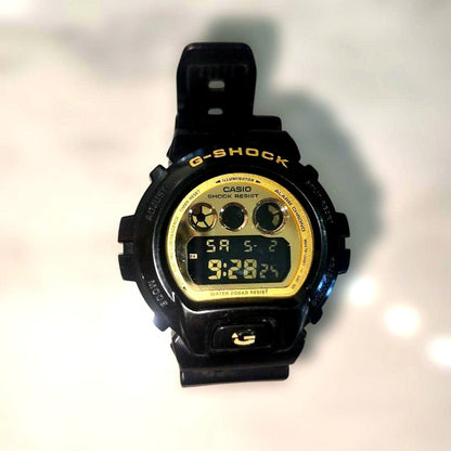 Casio G-Shock DW-6900CB black and gold watch with visible surface mark on G logo