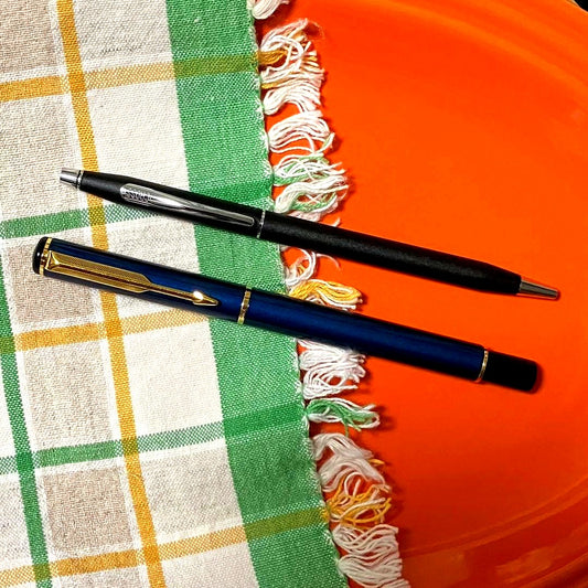 Cross black matte ballpoint pen with silver accents next to Parker blue and black fountain pen with gold nib engraving 88