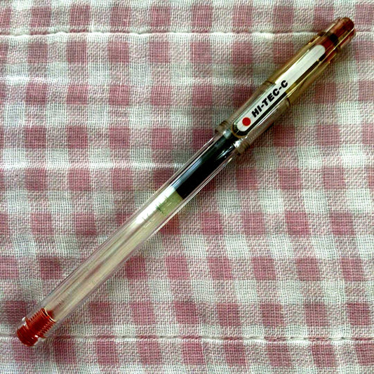 Pilot Hi-Tech C ballpoint pen in fluorescent brown with visible signs of wear and discoloration